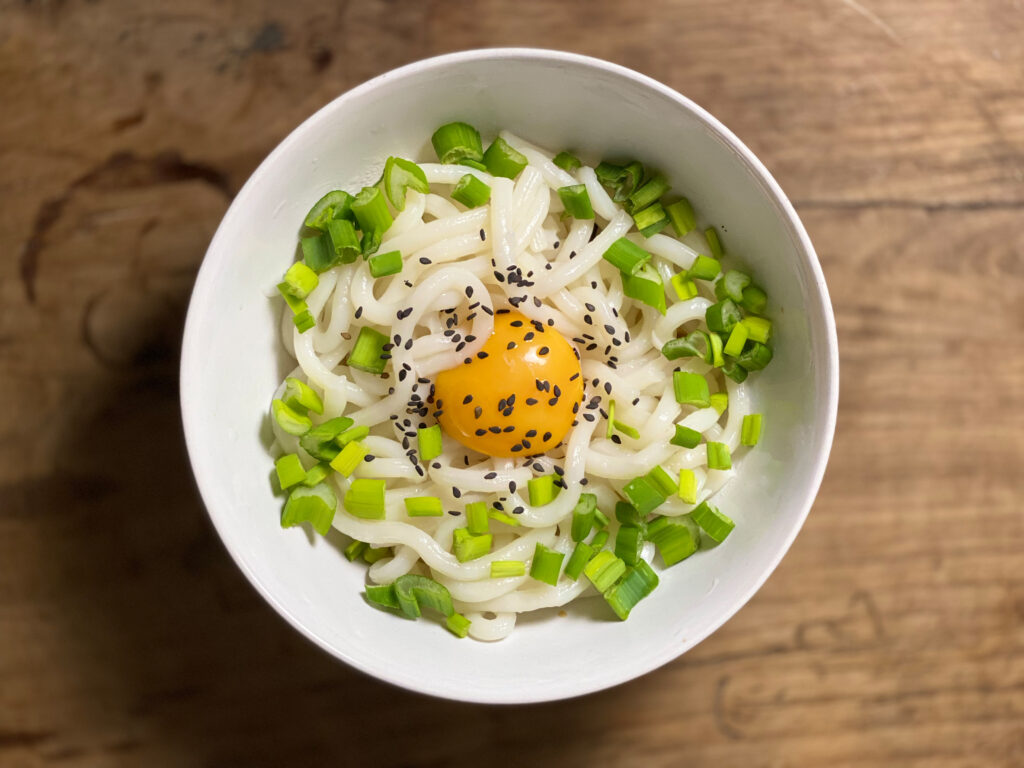 Kamatama Udon in a white bowel. Udon noodel, with fresh egg yolk and spring onions.
